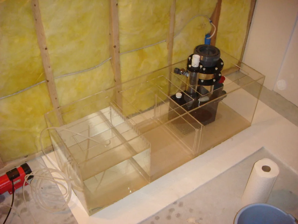 Empty three-chamber acrylic sump with a protein skimmer installed in the cabinet under a new marine aquarium