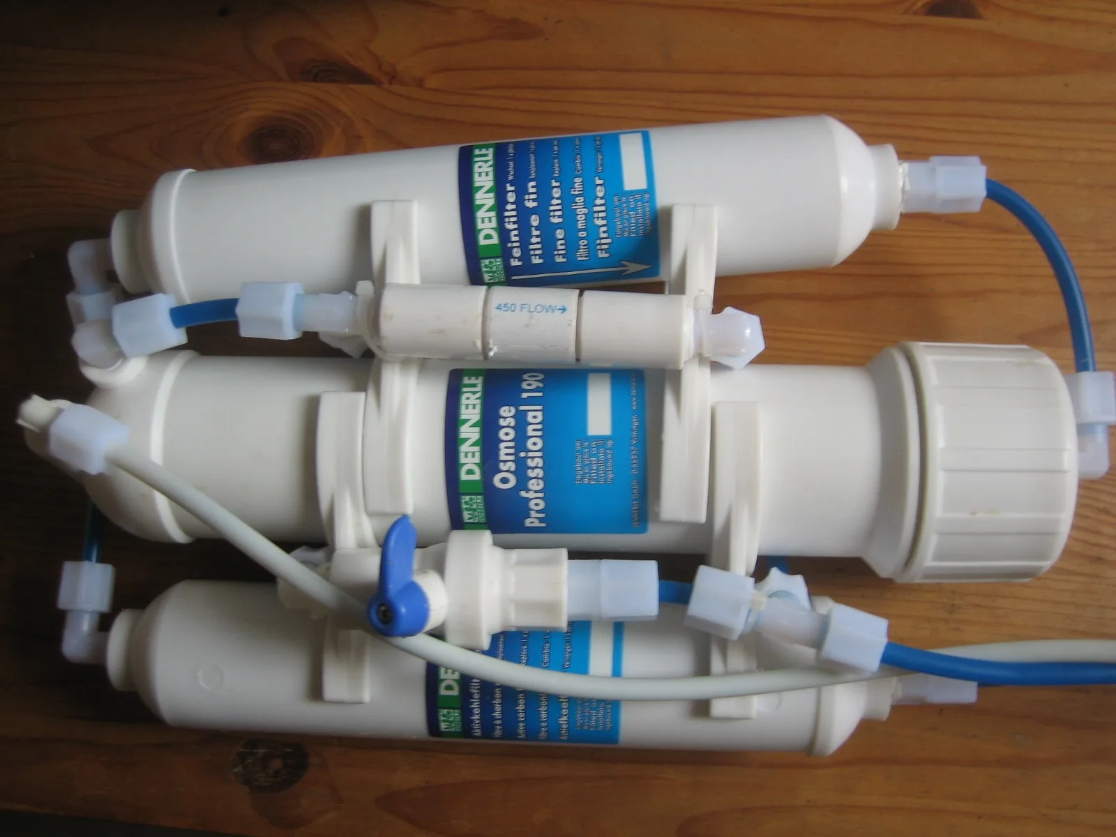 Reverse osmosis filter unit with three white housings and blue tubing laid on a wooden table